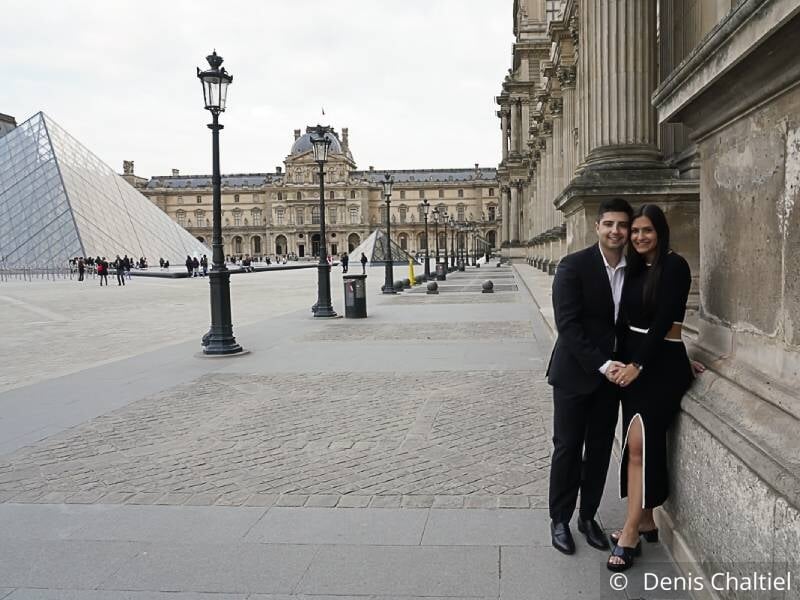 Un jeune couple enlacé sur la place du Louvre, avec la pyamide en fond.